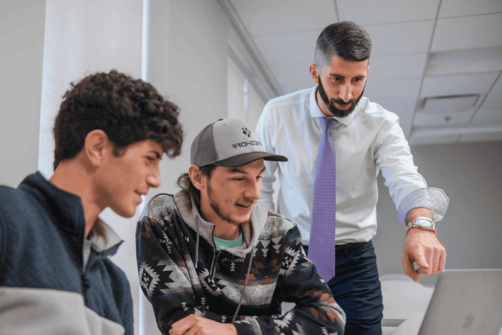 Students working together on a group project, guided by a teacher in a professional setting.